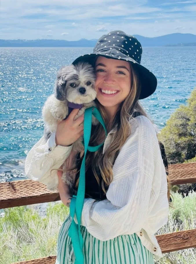 Ashley holding her small dog beside a lake